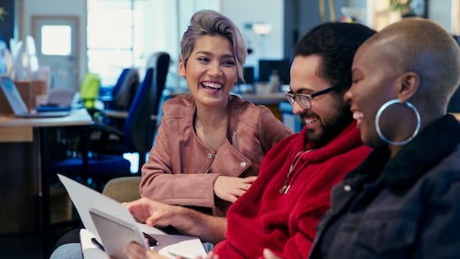 Three people in an office sitting together, looking at papers and laughing