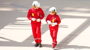 Male and female worker in red overalls and white helmets and hearing protection walking