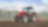 A red tractor ploughing a muddy field with trees in the background