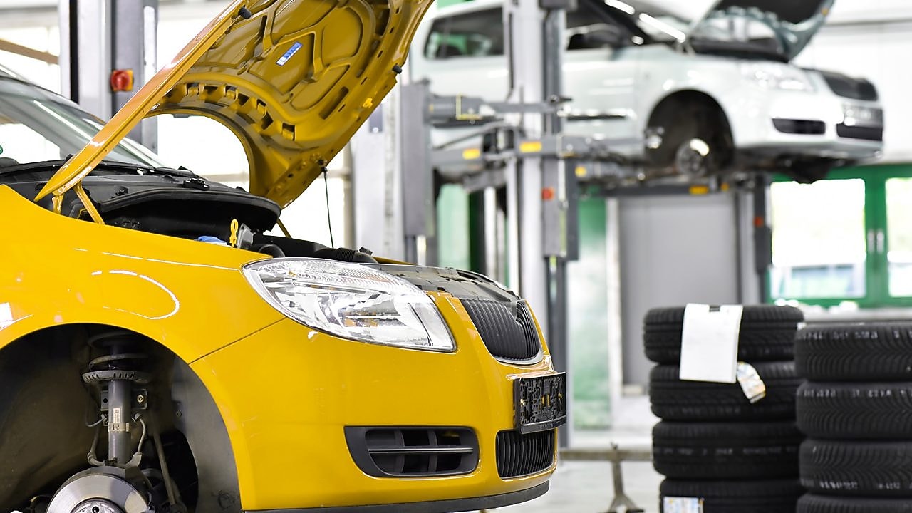 two cars in a garage, one yellow and one white, with their bonnets open, and some car tyres in the background