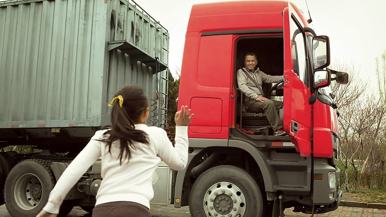 Man in red truck cab with door open waving to his daughter