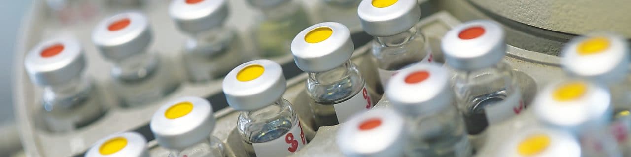 Rows of medicine vials sitting in a holder, some with red dots on the lid, and some with yellow dots on the lid
