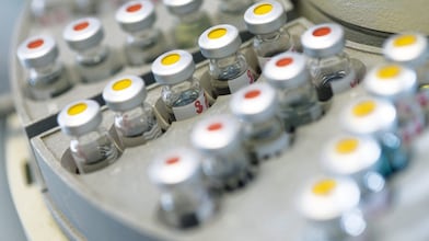 Rows of medicine vials sitting in a holder, some with red dots on the lid, and some with yellow dots on the lid