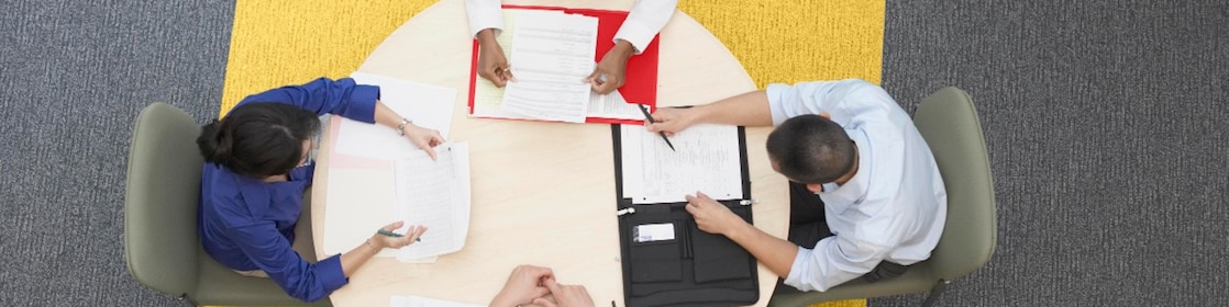 Four business people sitting around a round table reading documents, grey and yellow carpet