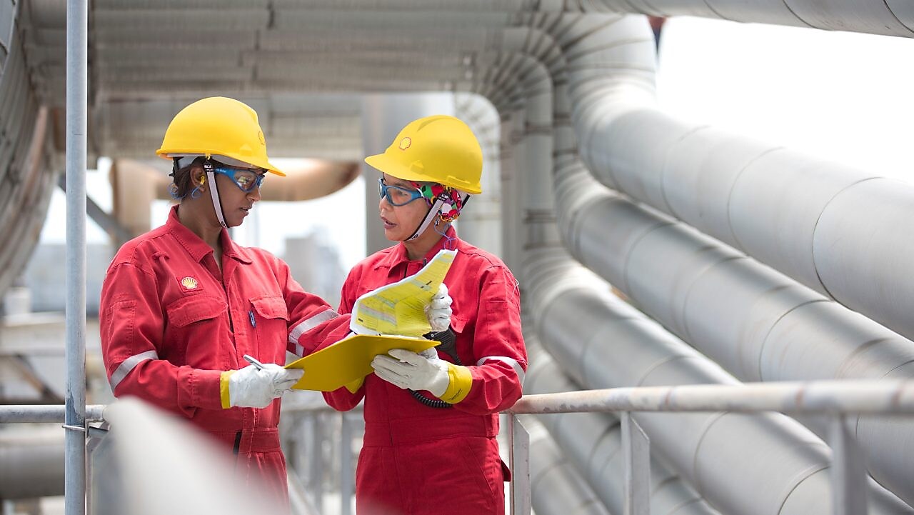Shot of two workers in hardhats discussing a project in a refinery
