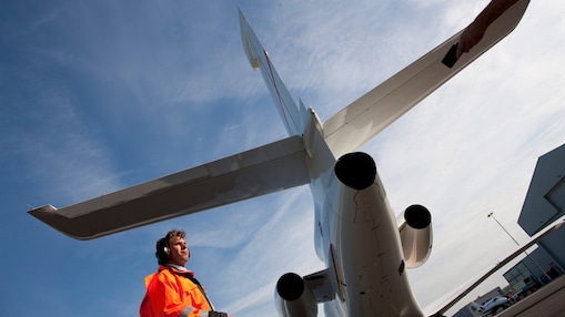 bottom up view of staff walking behind the tail end of a plane