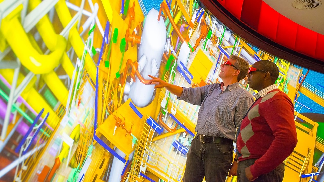 Two men use 3D glasses to look at a large colourful screen