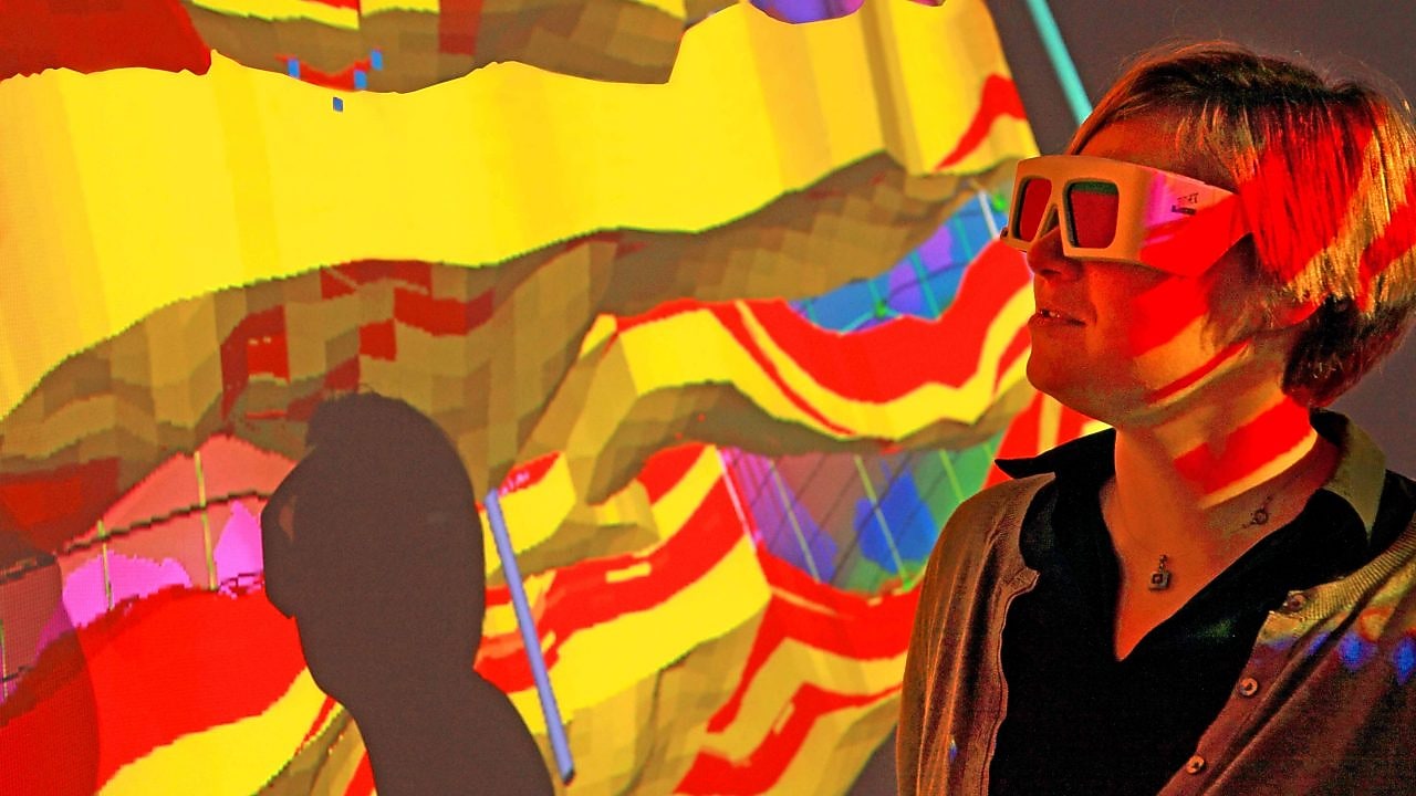 A woman with special goggles examines a 3D wall projection of a geological map 