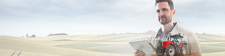 man reading a document with a background of fields and a red tractor