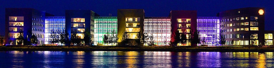 A set of lit office buildings reflect off the water at night